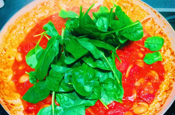 Add fresh spinach to the sauce and mix in before adding the cod to this Spanish One Pot national dish